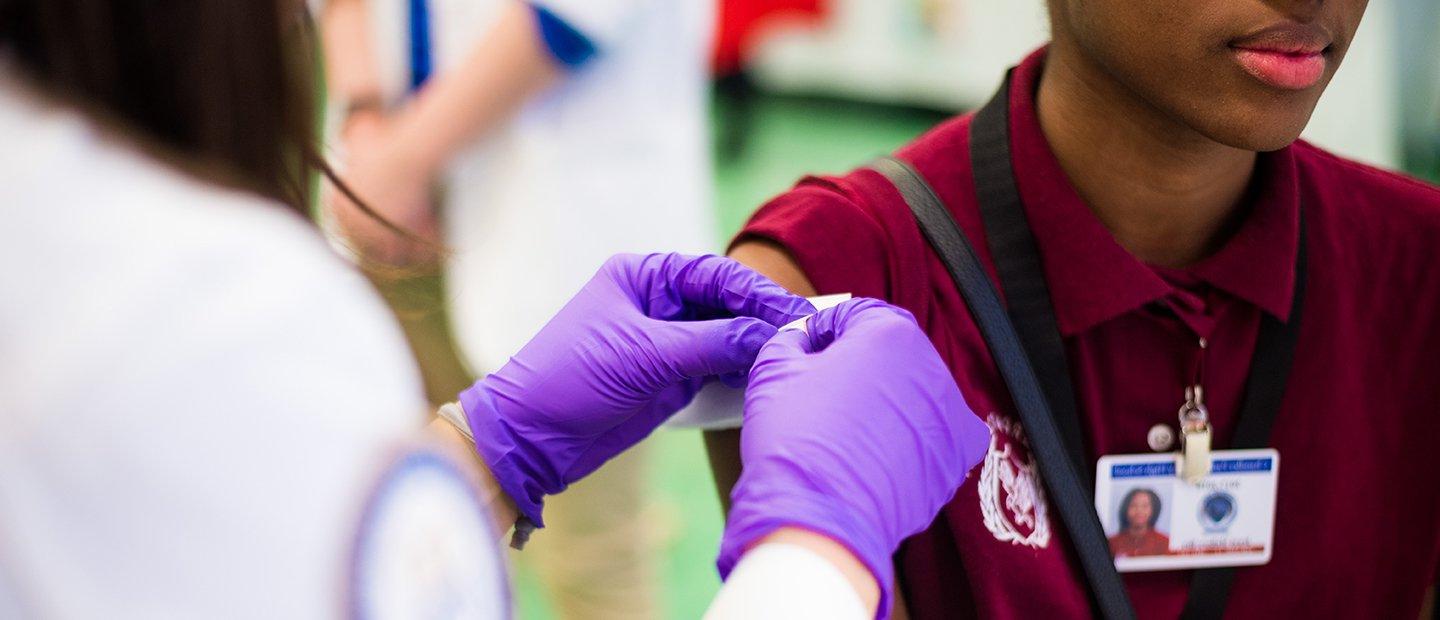 Person wearing purple medical gloves, applying a bandage to a person's arm.